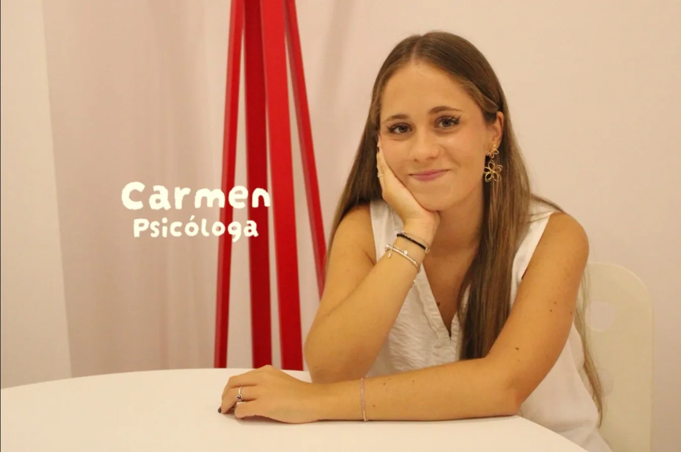 Carmen, psicóloga, sonriendo apoyada en una mesa blanca de la consulta