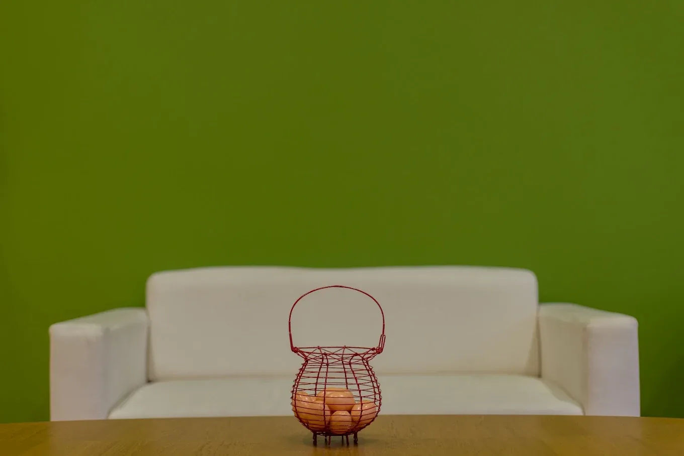Sofá blanco frente a una pared verde, con una cesta de mimbre sobre la mesa